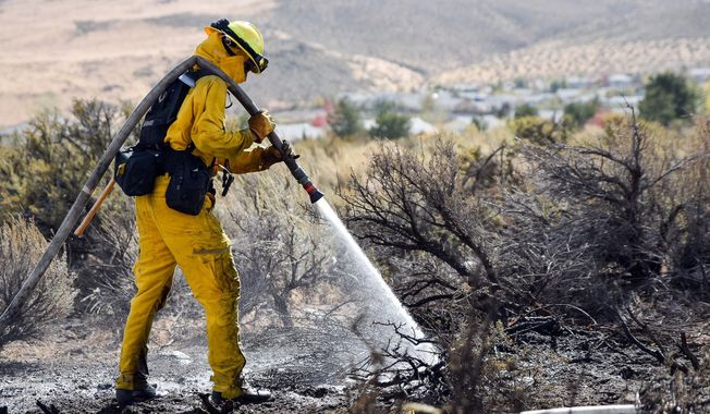 A firefighter hoses down the area on Mount Rose Highway and Edmonton Drive, Friday, Oct. 14, 2016 in Reno, Nev.. A wind-whipped wildfire raged out of control Friday in northern Nevada, destroying more than a dozen homes, forcing evacuations, closing roads and schools, and triggering power outages, officials said.(Mike Higdon/The Reno Gazette-Journal via AP)