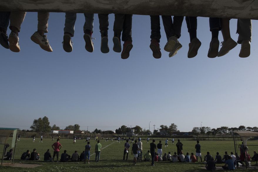 In this Friday, Oct. 14, 2016 photo, spectators watch a soccer match between refugee teams from Nea Kavala camp and Herso camp, in the village Nea Kavala northern Greece. Soccer players and fans from Syria and Iraq got a break from life at migrant camps to play a match organized by a government migration agency, launching a tournament that will include local amateur Greek teams. The first game on Friday was slow paced, with white lines on the pitch only half painted in. Spectators were seated on grass or on the terrace of a half-built home to get a decent view. (AP Photos/Giannis Papanikos)