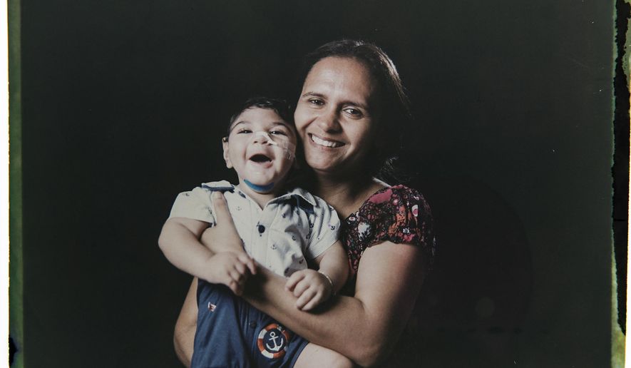 In this Sept. 29, 2016 photo made from a negative recovered from instant film, Rozilene Ferreira poses with her 1-year-old son, Arthur Conceicao, who was born with microcephaly, one of many serious medical problems that can be caused by congenital Zika syndrome, in Recife, Pernambuco state, Brazil. A year after a spike in the number of newborns with the defect known as microcephaly, Brazilian doctors and researchers have seen many of the babies develop swallowing difficulties, epileptic seizures and vision and hearing problems. (AP Photo/Felipe Dana)