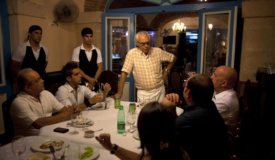 FILE - In this July 11, 2012 file photo, Tomas Erasmo Hernandez, center, owner of the private restaurant Mama Ines, chats with his customers in Old Havana, Cuba. Cuba is temporarily freezing new licenses for private restaurants in Havana, announced by acting Vice President Isabel Hamze on state media on Wednesday, Oct. 19, 2016. The city is also starting to impose more limits on private bed-and-breakfasts. (AP Photo/Ramon Espinosa, File)