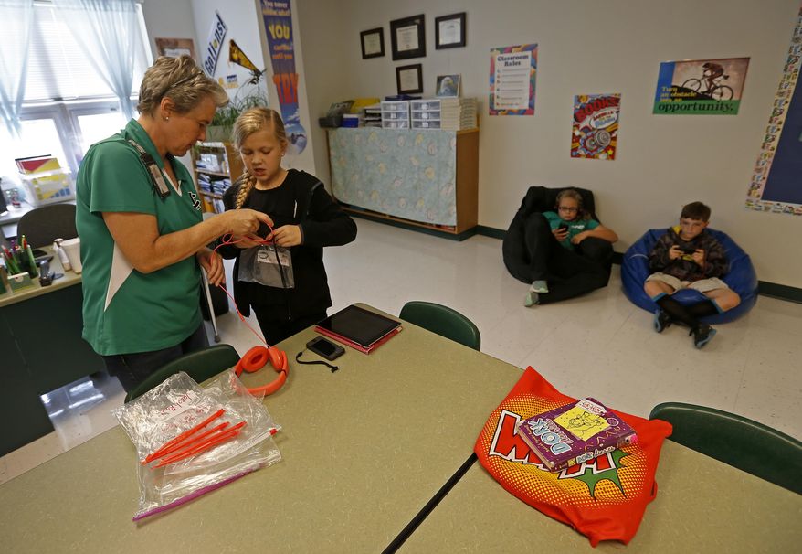 ADVANCE FOR USE SUNDAY, OCT. 23 - In this Thursday, Oct. 13, 2016 photo, teacher Leslie Patterson, left, helps her fourth-grade student Kaelynne Norlie check out an iPod to finish reading a book using the Voice Dream Reader app on a desktop computer in the library at Kathryn Griffis Elementary in Caddo Mills, Texas. The text-to-speech app is a tool that helps print-disabled students listen to articles while reading books on any devices with the app installed. (Jae S. Lee/The Dallas Morning News via AP)