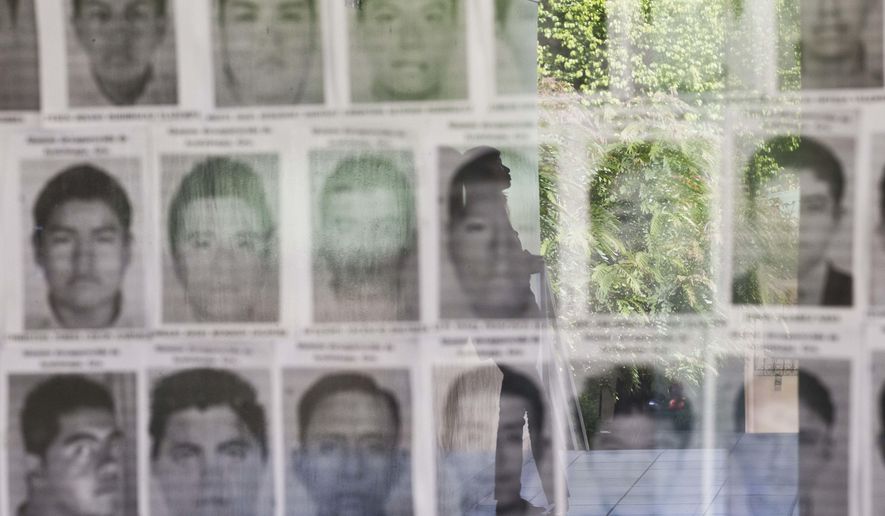 FILE - In this Nov. 18, 2014 file photo, a university student is reflected in a glass display case showing the photos of 43 missing students from the Rural Normal School of Ayotzinapa, Mexico, at the Central American University, UCA, in Managua, Nicaragua. Mexican authorities announced they detained on Friday, Oct. 21, 2016 the former police chief of Iguala where the students disappeared on Sept. 26, 2014. The students were taken by police and have not been heard from since. (AP Photo/Esteban Felix, File)