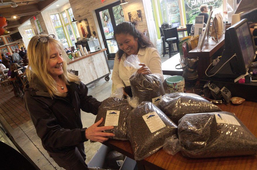 In this Thursday, Oct. 6, 2016 photo, Bainbridge Island resident Carol Carley , left, helps Ometepe Island resident Dora Gutierrez unload coffee beans, which were grown on the Nicaraguan island, at The Marketplace at Pleasant Beach on Bainbridge Island, Wash. Since 1988 more than than 500,000 pounds of Ometepe coffee have been sold on Bainbridge. (Nathan Pilling/Kitsap Sun via AP)