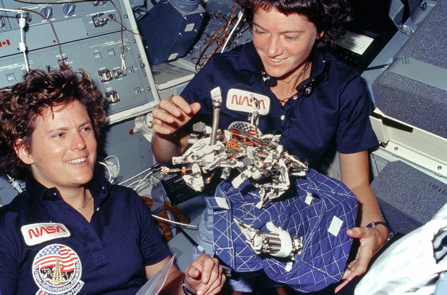 Astronauts Kathryn D. Sullivan, left, and Sally K. Ride display a "bag of worms." The "bag" is a sleep restraint and the majority of the "worms" are springs and clips used with the sleep restraint in its normal application. Clamps, a bungee cord and velcro strips are other recognizable items in the "bag. October 6, 1984