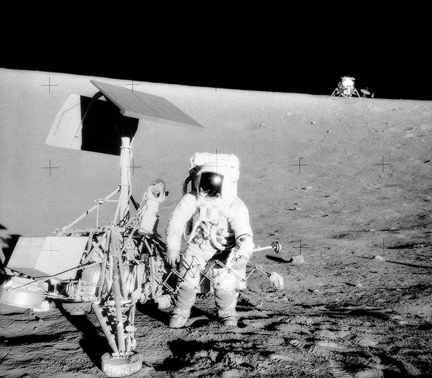Charles Conrad Jr., Apollo 12 Commander, examines the unmanned Surveyor III spacecraft during the second extravehicular activity (EVA-2). The Lunar Module (LM) "Intrepid" is in the right background. This picture was taken by astronaut Alan L. Bean, Lunar Module pilot. The "Intrepid" landed on the Moon's Ocean of Storms only 600 feet from Surveyor III. The television camera and several other components were taken from Surveyor III and brought back to earth for scientific analysis. Surveyor III soft-landed on the Moon on April 19, 1967.