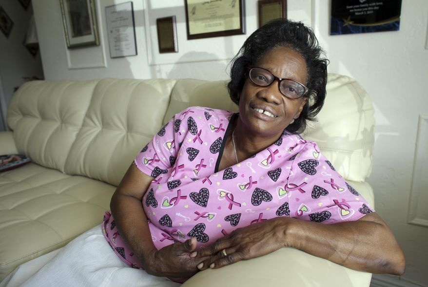 In this photo taken Oct. 18, 2016, Gwen Strowbridge, 71, poses for a photograph wearing her work uniform at her home in Deerfield Beach, Fla. Strowbridge works six days a week caring for a 100-year-old woman. She has worked all her life and plans to work until she can't physically work anymore. (AP Photo/Lynne Sladky)