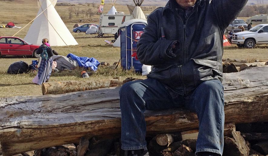 Loren Bagola, from the Cheyenne River Reservation in South Dakota, helps handle security Monday, Oct. 24, 2016, at the Dakota Access oil pipeline protest in southern North Dakota. Bagola is sitting atop a pile of logs that protesters prepared to use to block a highway. The long-running dispute over the Dakota Access oil pipeline expanded to private land recently purchased by the pipeline builders, with protesters who say the area rightfully belongs to Native Americans setting up camp and vowing to stay put until the project is stopped. (AP Photo/Blake Nicholson)
