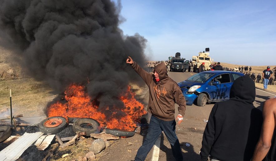 Demonstrators stand next to burning tires as armed soldiers and law enforcement officers assemble on Thursday, Oct. 27, 2016, to force Dakota Access pipeline protesters off private land where they had camped to block construction. The pipeline is to carry oil from western North Dakota through South Dakota and Iowa to an existing pipeline in Patoka, Ill. (Mike McCleary/The Bismarck Tribune via AP)
