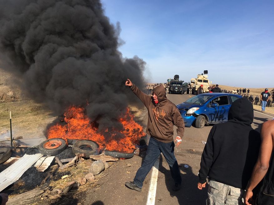 Demonstrators stand next to burning tires as armed soldiers and law enforcement officers assemble on Thursday, Oct. 27, 2016, to force Dakota Access pipeline protesters off private land where they had camped to block construction. The pipeline is to carry oil from western North Dakota through South Dakota and Iowa to an existing pipeline in Patoka, Ill. (Mike McCleary/The Bismarck Tribune via AP)