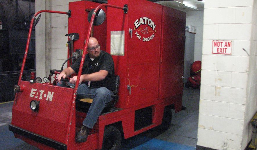 In this undated photo, Kearney Eaton Corp. training coordinator Elias Bules pulls the miniature fire truck out of a small station inside the plant in Kearney, Neb.. The truck is equipped with bunker gear, hoses, extinguishers and SCBA's (self-contained breathing apparatus) for firefighters. The truck runs on propane and carries medical supplies, including an automated external defibrillator. (Kim Schmidt/The Daily Hub via AP)