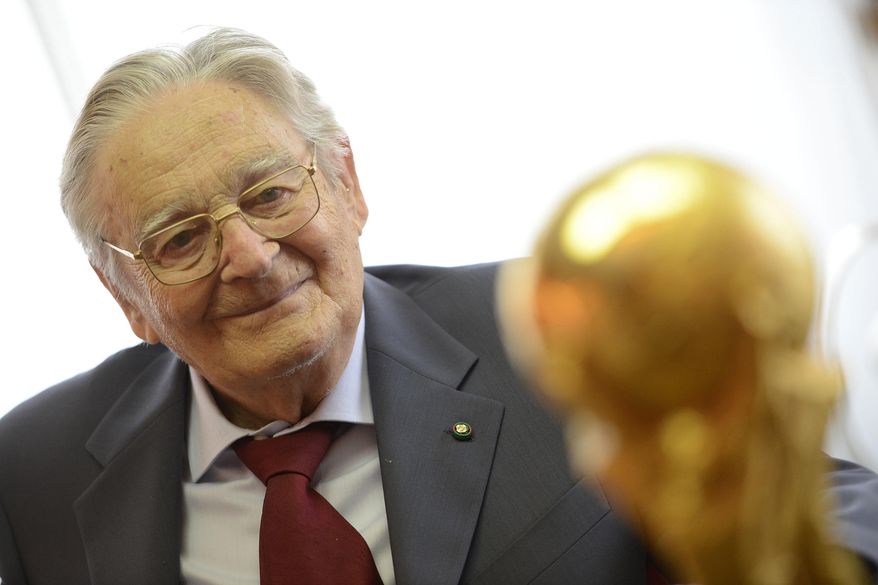 In this photo taken on Thursday, June 3, 2014, Italian goldsmith and sculptor Silvio Gazzaniga poses with his most important work, the FIFA World Cup at GDE Bertoni factory in Paderno Dugnano, near Milan, Italy. Silvio Gazzaniga, the sculptor who created the World Cup trophy, has died. He was 95. Gazzaniga designed and created the World Cup trophy in 1971 after Brazil retained the right to keep the Jules Rimet trophy by winning its third World Cup in 1970. (AP Photo/Giuseppe Aresu)