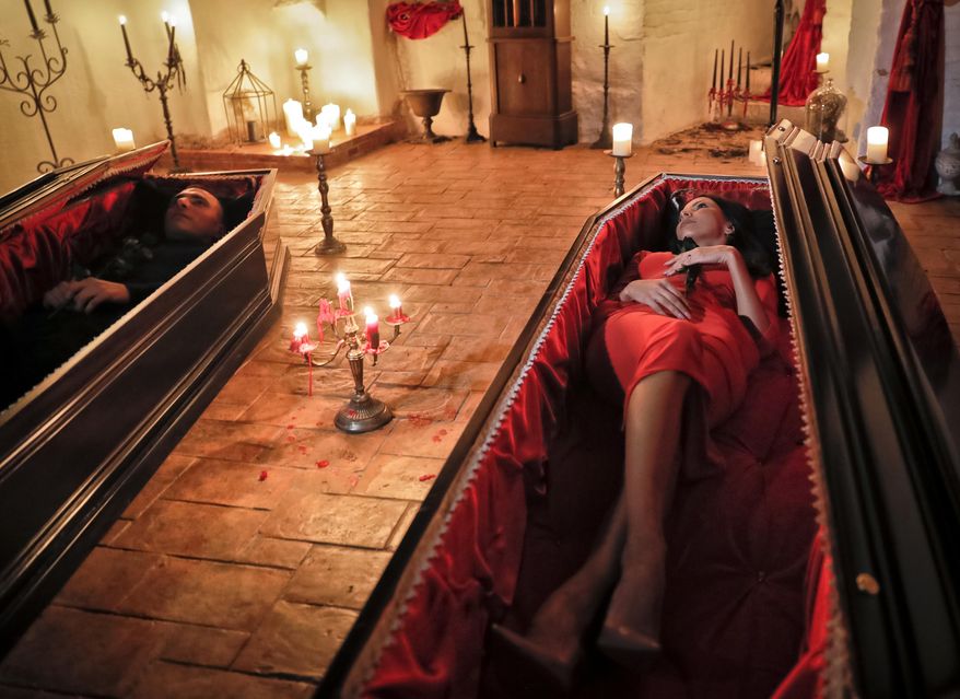 Tami Varma, right, and her brother Robin, the grandchildren of Devendra Varma, a scholar of English gothic tales and an expert in vampire lore, pose in coffins at the Bran Castle, in Bran, Romania, Monday, Oct. 31, 2016. A Canadian brother and sister are passing Halloween night curled up in red velvet coffins in the Transylvanian castle that inspired the Dracula legend, the first time in 70 years anyone has spent the night in the gothic fortress, after they bested 88,000 people who entered a competition hosted by Airbnb to get the chance to dine and sleep at the castle in Romania. A portrait of medieval prince Vlad the Impaler is placed on the wall. (AP Photo/Vadim Ghirda)