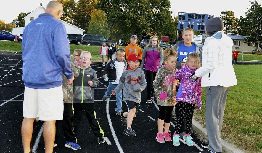 In this Oct. 4, 2016 photo, Blue Hill Public Schools teachers Jon Coffey and Kaitlyn Wright punch cards for students participating in the walk/run club before school on the track in Blue Hill, Neb. (Susan Danehey/The Hastings Tribune via AP)
