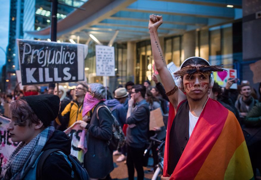 A young man draped in a rainbow flag raises his fist as he and other protesters hold a rally against U.S. President-elect Donald Trump outside the still under construction Trump Hotel, in Vancouver, British Columiba, Thursday, Nov. 10, 2016. (Darryl Dyck/The Canadian Press via AP)