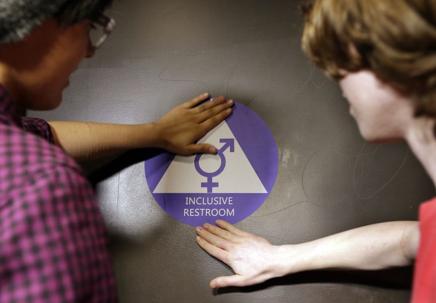 Students place a new sticker on the door at the ceremonial opening of a gender-neutral bathroom at Nathan Hale High School on May 17 in Seattle. (Associated Press) **FILE**