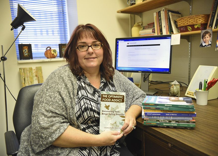 ADVANCE FOR WEEKEND EDITIONS - In this Thursday, Oct. 13, 2016, photo, Dr. Christina Fisanick-Greer holds her most recent book, released in October, that deals with her life as a binge eater and her recovery, in her office at California University in California, Pa. (Celeste Van Kirk/Observer-Reporter via AP)