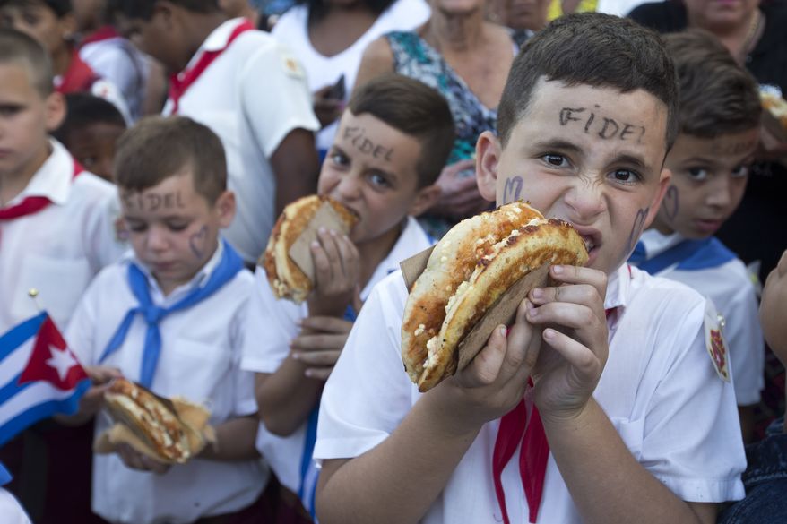 School boys eat pizza as they line to see the ashes of Cuba's leader Fidel Castro being carried in a funeral procession on its way to the east of te country in Florida, Cuba, Thursday, Dec. 1, 2016. Castro's ashes are in a four-day journey across Cuba from Havana to their final resting place in the eastern city of Santiago. (AP Photo/Ricardo Mazalan)