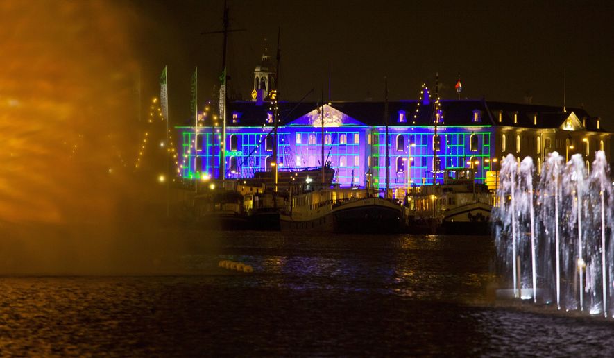 Blue Print by Dutch light designer Reier Pos is seen projected on the Nautical Museum, rear, as Arco, an art work by Austrian artist Teresa Mar is seen in the foreground, both installations are part of the Amsterdam Light Festival, Netherlands, Wednesday, Nov. 30, 2016. The festival opens on Dec. 1, 2016, and ends on Jan. 22, 2017, the artworks are lit from 17:00 until 23:00, and for the Illuminade, a walking route, between 17:00 and 22:00 Central European Time. (AP Photo/Peter Dejong)