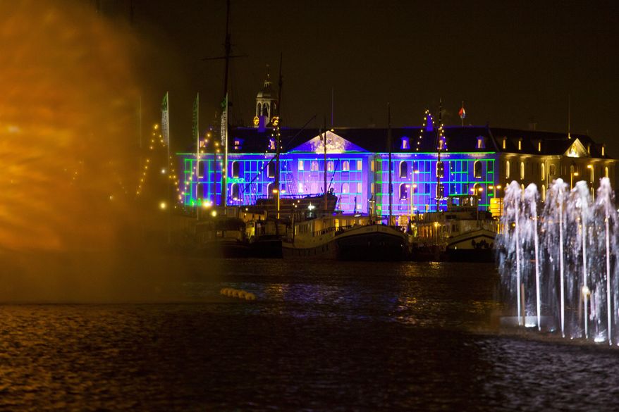 Blue Print by Dutch light designer Reier Pos is seen projected on the Nautical Museum, rear, as Arco, an art work by Austrian artist Teresa Mar is seen in the foreground, both installations are part of the Amsterdam Light Festival, Netherlands, Wednesday, Nov. 30, 2016. The festival opens on Dec. 1, 2016, and ends on Jan. 22, 2017, the artworks are lit from 17:00 until 23:00, and for the Illuminade, a walking route, between 17:00 and 22:00 Central European Time. (AP Photo/Peter Dejong)