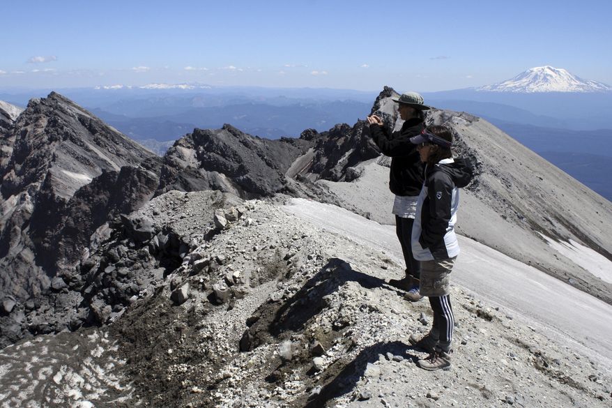 ADVANCE FOR USE SATURDAY, DEC. 3 - FILE - In this July 9, 2013, file photo, Kristen Hill and Michele Walker Richardson take photos from Mount St. Helens' crater rim in Washington state on with Mount Adams is the background. Visitors will have the opportunity to explore Mount St. Helens in a variety of ways throughout 2017, thanks to programs offered by the Mount St. Helens Institute. (Craig Hill/The News Tribune via AP, File)