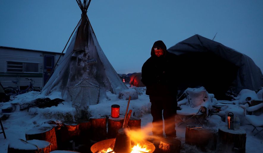 James Logan, a Northern Arapaho Native American from Wyoming and pipeline protester, warms himself by a fire. Activists have vowed to stay in the camps, even after the Obama administration blocked the pipeline, and the chairman of the Standing Rock Sioux tribe has asked non-native protestors to leave. (Associated Press)