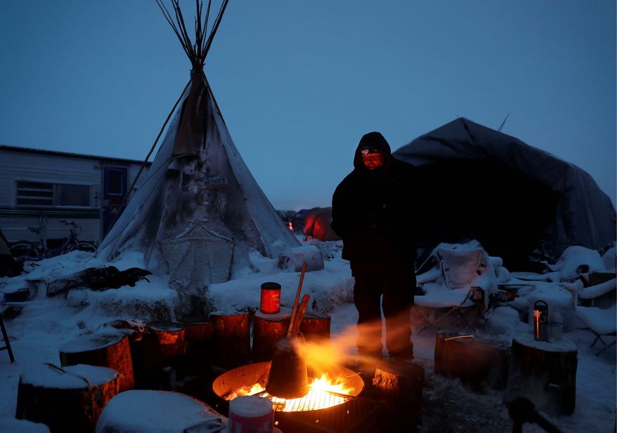 James Logan, a Northern Arapaho Native American from Wyoming and pipeline protester, warms himself by a fire. Activists have vowed to stay in the camps, even after the Obama administration blocked the pipeline, and the chairman of the Standing Rock Sioux tribe has asked non-native protestors to leave. (Associated Press)