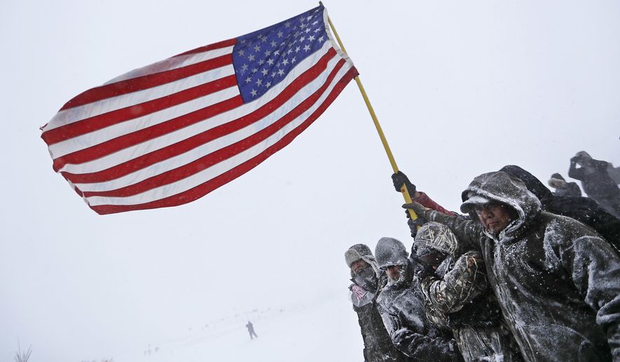 Military veterans huddle together to hold an American flag against strong winds during a march to a closed bridge outside the Oceti Sakowin camp where people have gathered to protest the Dakota Access oil pipeline in Cannon Ball, N.D., Monday, Dec. 5, 2016. (AP Photo/David Goldman)