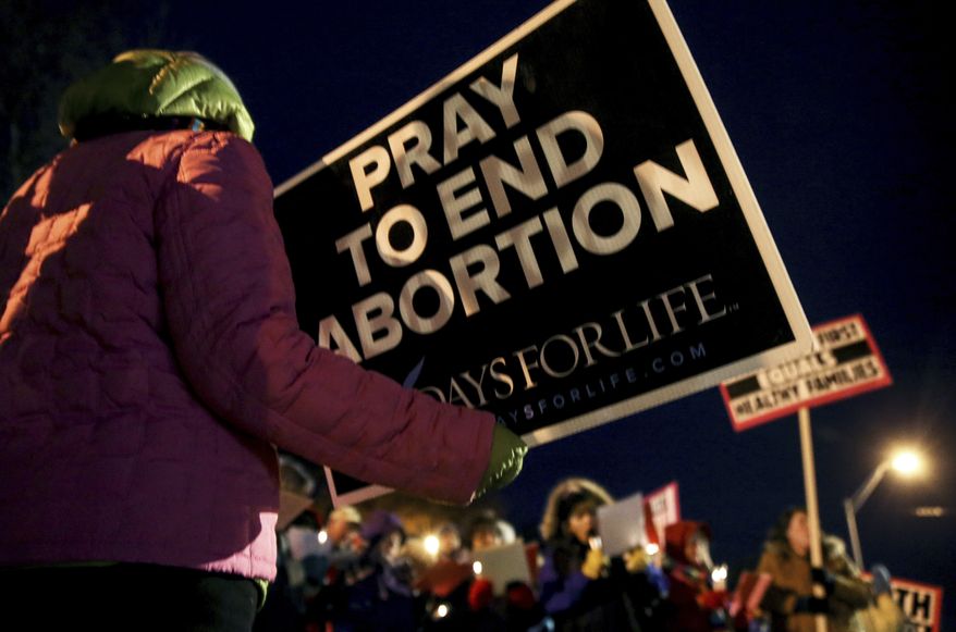 Mary Hoffmeyer, of Taos, Mo., holds a sign as she and other anti-abortion advocates sing Christmas carols after attending a news conference accusing Planned Parenthood facilities of being unsafe outside the Planned Parenthood Columbia Health Center on Monday, Dec. 12, 2016 in Columbia, Mo. The news conference was one of five held simultaneously outside Planned Parenthood locations across the state in which anti-abortion advocates argued that the number of ambulance calls to the St. Louis clinic since 2009 was cause for concern. (Timothy Tai/Columbia Daily Tribune via AP)