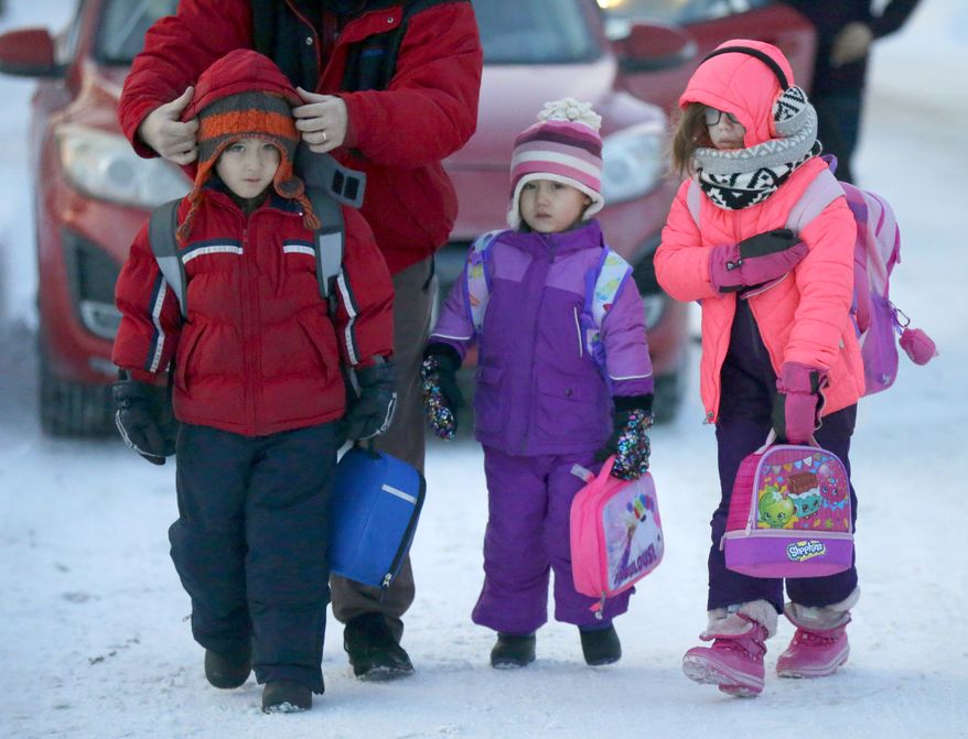 Reese Orr, far left, has his hat secured by his father, Chad Orr, of Milwaukee, as they and Orr's sister, Macy Rea Orr, center, and friend Eleanore Lawton, walk into school at John Greenleaf Whittier Elementary School, in Milwaukee, Wis., on Tuesday, Dec. 13, 2016. Overnight Monday into Tuesday, a blast of arctic air blew into Wisconsin and is dropping temperatures to dangerous levels. The bitterly cold air will settle into southern Wisconsin Tuesday through Friday. (Mike De Sisti /Milwaukee Journal-Sentinel via AP)
