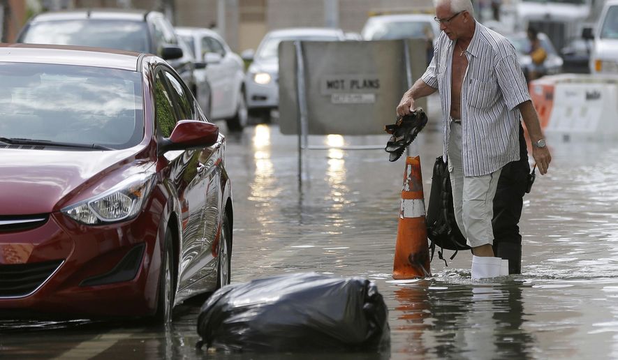 FILE - In this Sept. 30, 2015 file photo, a hotel guest carries his shoes as he is escorted to his car along in Miami Beach, Fla. The street flooding was in part caused by high tides due to the lunar cycle, according to the National Weather Service. A new scientific report finds man-made climate change played some kind of role in two dozen extreme weather events around the world in 2015. But it also detected no global warming fingerprints in a handful of other weird weather instances. (AP Photo/Lynne Sladky, File)