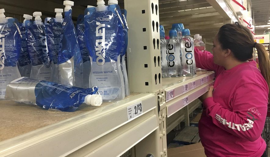 In this Thursday, Dec. 15, 2016 photo, a woman reaches for bottles of water after a recent back-flow incident in the industrial district according to a city news release, at H-E-B in Corpus Christi, Texas. (Gabe Hernandez/Corpus Christi Caller-Times via AP)