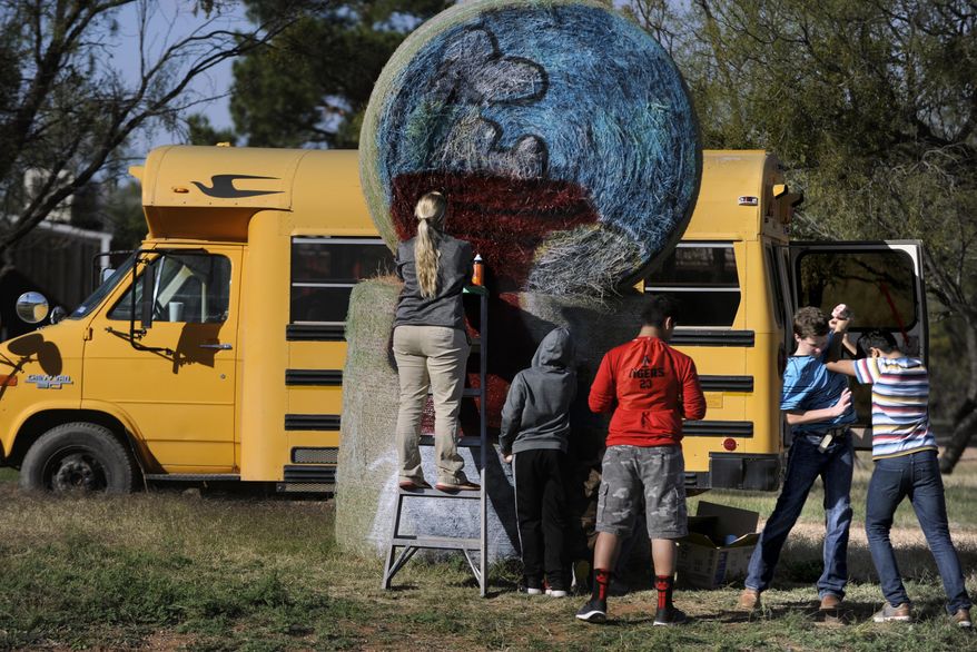 ADVANCE FOR USE SUNDAY, DEC. 18 - In this Nov. 29, 2016 photo, a pair of boys momentarily wrestle as they pass each other while Erica Jones adds color to the hay bale painting of Snoopy's doghous in Anson, Texas. Anson Middle School art students have painted 41 bales around town for the Christmas season. (Ronald W. Erdrich/The Abilene Reporter-News via AP)