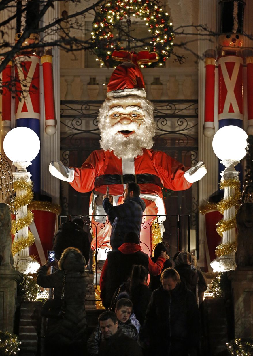 In this Dec. 15, 2016, photo, a giant animatronic Santa Claus towers over tourists taking photos at the elaborately-decorated Polizotto mansion in Dyker Heights neighborhood in the Brooklyn Borough of New York. The neighborhood has been drawing more tourists each year to see spectacular displays of Christmas lights and decorations like this one. (AP Photo/Kathy Willens)