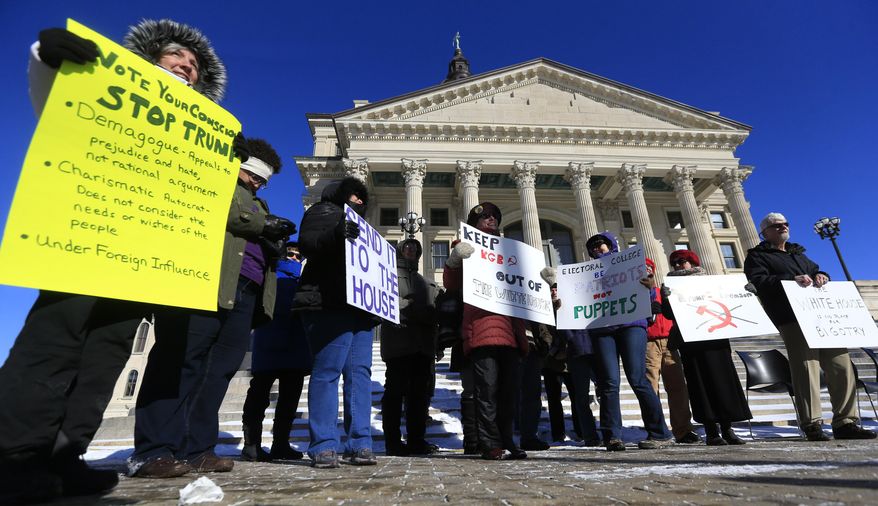 Protesters against President-elect Donald Trump hold signs outside the Kansas Statehouse in Topeka, Kan., Monday, Dec. 19, 2016. Six electors of the Electoral College will cast their votes inside the Senate chambers. (AP Photo/Orlin Wagner)