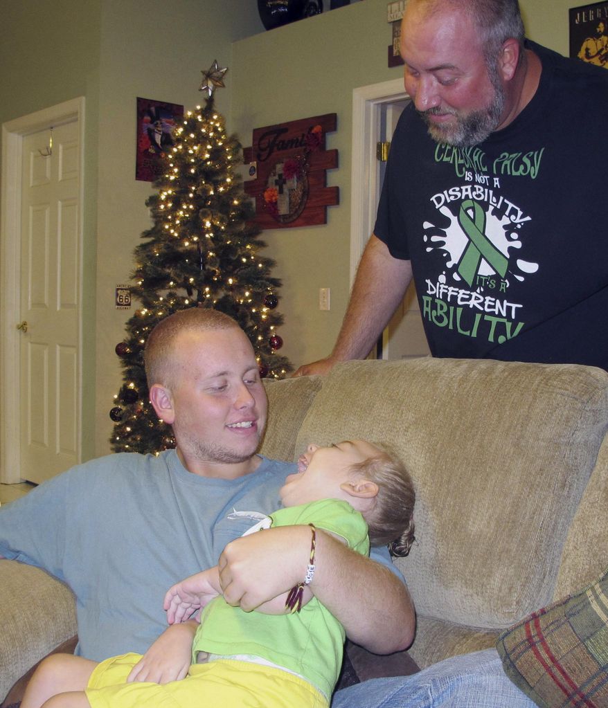 In this Thursday, Dec. 1, 2016, photo, Scarlett Wilgis, bottom, is held by her brother Joey McKinley, 17, while her father Herman Wilgis observes them in St. Augustine, Fla. Because of her cerebral palsy, 4-year-old Scarlett has trouble opening her hands and can't get around without help. Her parents have scoured store shelves and websites looking for toys for her, but have mostly been disappointed. Scarlett and her family are part of the Adaptive Toy Program at the University of North Florida, which assigns engineering and physical therapy students to convert drivable toy cars from store shelves into custom-made fun for disabled children. (AP Photo/Jason Dearen)