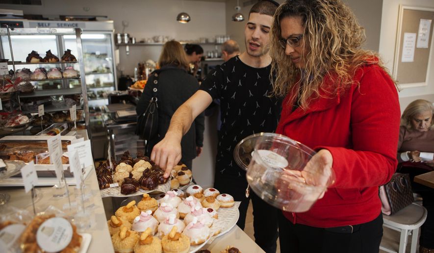In this Thursday, Dec. 15, 2016 photo, a bakery employee helps customer choose doughnuts in Bnei Brak, Israel. Israelis are finding new advice hard to swallow: in the name of proper nutrition, their health minister has gone on the warpath against the beloved Hanukkah tradition of gorging on sugar-laden, deep-fried, jam-filled doughnuts. Yaakov Litzman _ the bearded, black-coated chief of a powerful ultra-Orthodox political party _ considers himself a guardian of Jewish traditions. But he also wears another hat, as a health conscious official on a crusade to stamp out junk food and child obesity. (AP Photo/Dan Balilty)