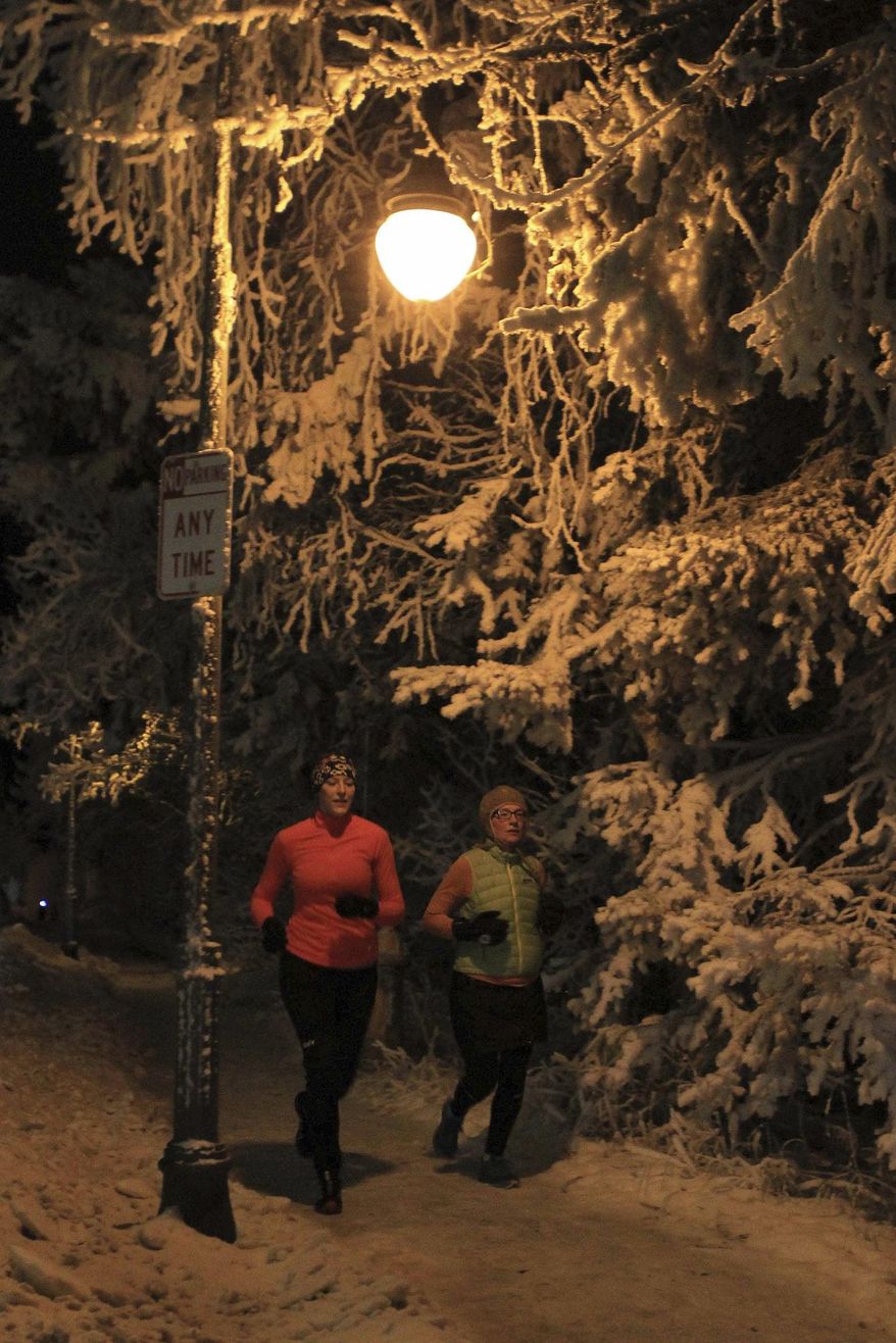 In this Tuesday, Dec. 14, 2016, photo, runners jog under snowy branches and a street light on a Second Avenue sidewalk in Anchorage, Alaska With ice present on city streets for up to seven months per year, most Anchorage walkers and runners use footwear that has built-in studs or attached cleats as a safety measure to avoid falling. (AP Photo/Dan Joling)