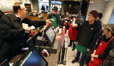 In this Dec. 19, 2016, Father Jim Sichko handed out a $100 bills to employees at a Starbucks in Lexington, Ky. Sichko paid out about $6,000 in holiday good will to a Starbucks counter crew, a Muslim refugee family, a Hispanic family with a desperately ill father and an LGBT man who needed help with groceries for himself and his mother. (Charles Bertram/Lexington Herald-Leader via AP)