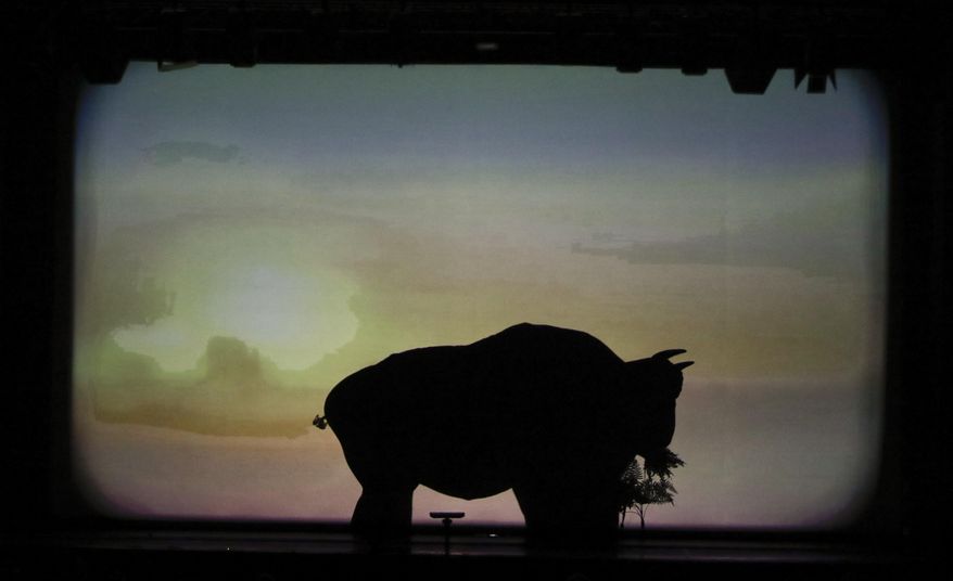 In this photo taken Tuesday, Dec. 20, 2016, dancers of the U.S. company 'Catapult' create a buffalo eating in a field, during their show 'Magic Shadows', in Milan, Italy. Dancers in the company create shadow sculptures with their bodies, giving a contemporary twist to the ancient Chinese art of shadow theaters. (AP Photo/Luca Bruno)