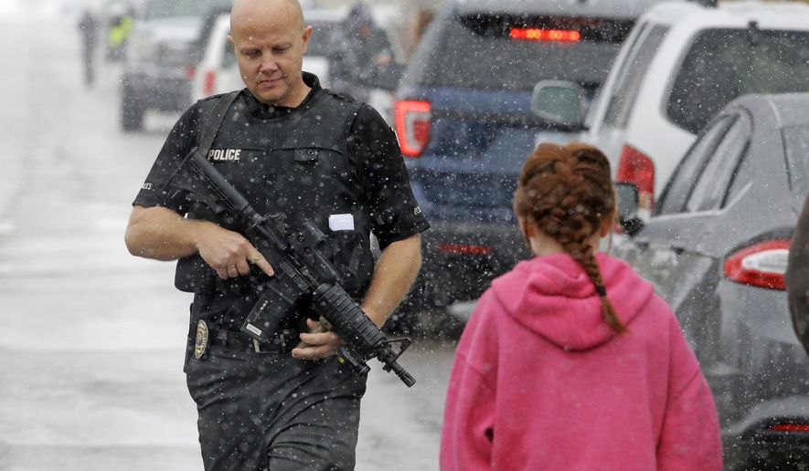 FILE - This Dec. 1, 2016, file photo, a police officer carries his weapon as he walks along the street in front of Mueller Park Junior High after a student fired a gun into the ceiling, in Bountiful, Utah. Police said a 15-year-old brought two guns to school and fired a round into a classroom ceiling before his parents arrived and disarmed him, likely preventing bloodshed. A series of violent crimes involving teenage suspects over the last two months is raising tough questions for Utah courts, police and parents. (AP Photo/Rick Bowmer, File)