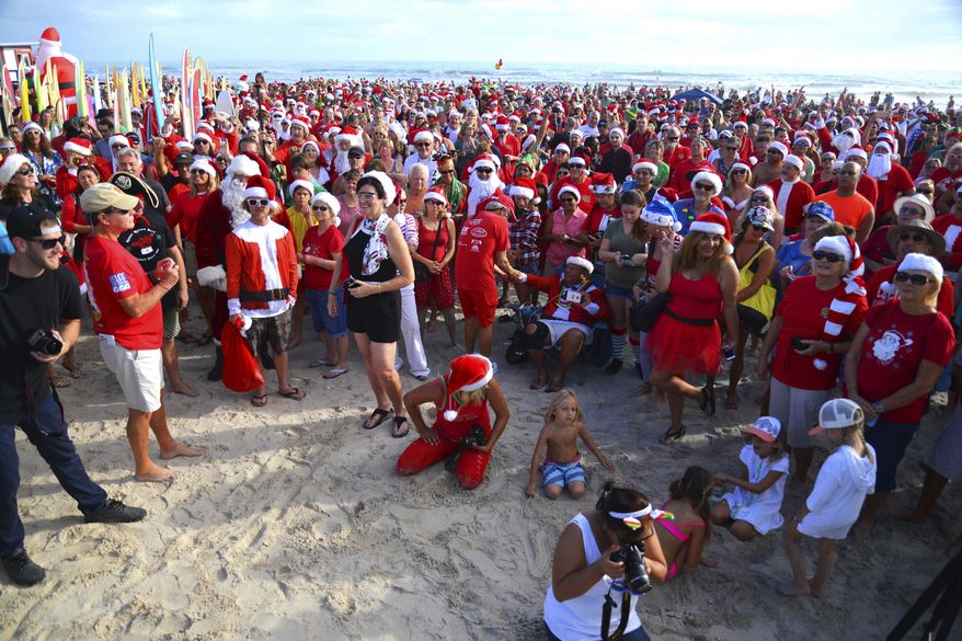 Thousands gather to watch hundreds of surfing Santas hit the waves during an event in Cocoa Beach, Fla., Saturday, Dec. 24, 2016. The Christmas event supports Grind for Life and the Surf Museum. (Malcolm Denemark/Florida Today via AP)