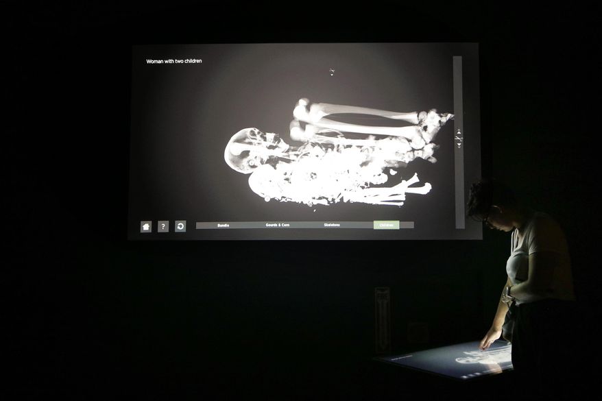 FILE - In this Sept. 10, 2015, file photo, Alexis Hyde, right, looks at an interactive display of a CT scan from a Peruvian mummy of a woman with two children at the Natural History Museum, in Los Angeles. It is part of a traveling exhibition that used CT scanning to "unwrap" ancient mummies and is an example of museums working to present exciting and meaningful exhibits by increasingly relying on technology. (AP Photo/Jae C. Hong, File)