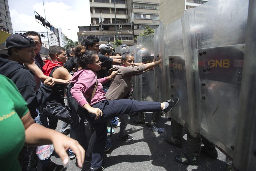 FILE - In this June 2, 2016 file photo, a woman kicks National Guard soldiers' shields during a protest demanding food, near Miraflores presidential palace in Caracas, Venezuela, triggered by rising frustration with food shortages and inflation. President Nicolas Maduro has greatly enhanced the power of his generals, who have become an indispensable crutch as the economy has tanked and street protests against the deeply-unpopular administration grow. (AP Photo/Ariana Cubillos, File)