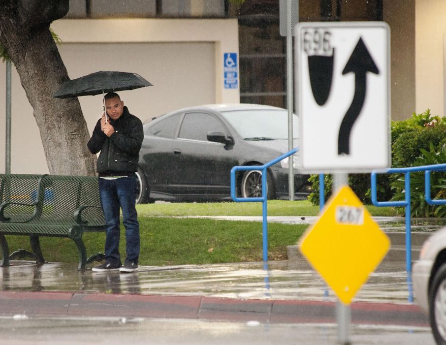 A man makes a call under his umbrella as he waits at a N. St. College Blvd. bus stop as a light, warm rain falls Friday morning, Dec. 30, 2016, in Anaheim.California's wet December is drawing to a close with even more rain and snow in a welcome respite amid years of drought. A warm low-pressure storm system brought showers to Southern California starting early Friday and slowly moved east through the day as a cold weather system dropped down toward the state from the north. (Ken Steinhardt/The Orange County Register via AP)