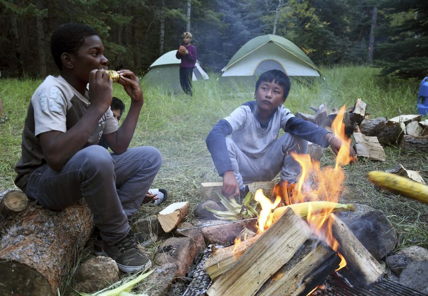 In this Sept. 10, 2016, photo, Justin Mbelechi, 13, and Bidesh Magar, 14, roast corn at their campsite in Evergreen, Colo. The two belong to a Colorado Boy Scout troop that is made up almost entirely of refugees. At campouts, traditional American food like hot dogs and trail burgers is replaced by fish head stew, fire-roasted corn and Chatpate, a popular Nepalese street snack. (AP Photo/Thomas Peipert)