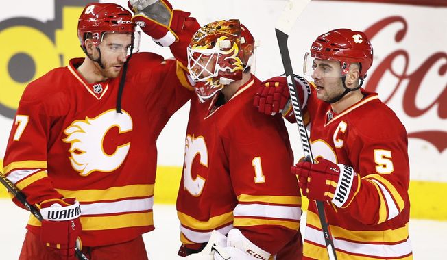 Calgary Flames goalie Brian Elliott, center, is congratulated by TJ Brodie, left, and Mark Giordano celebrate the team's 4-2 victory over the Arizona Coyotes in an NHL hockey game Saturday, Dec. 31, 2016, in Calgary, Alberta. (Larry MacDougal/The Canadian Press via AP)