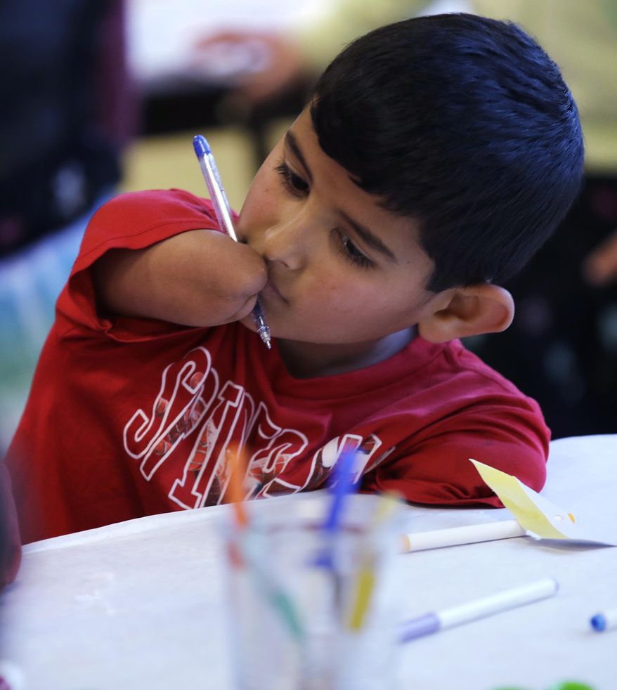 In this Dec. 10, 2016 photo, Syrian refugee Ahmad Alkhalaf pauses prior to making a card for refugee children displaced in Syria during a day camp for local Muslim children in Sharon, Mass. The young boy who lost his arms in a refugee camp bomb blast is thriving in his new life in Massachusetts. (AP Photo/Charles Krupa)