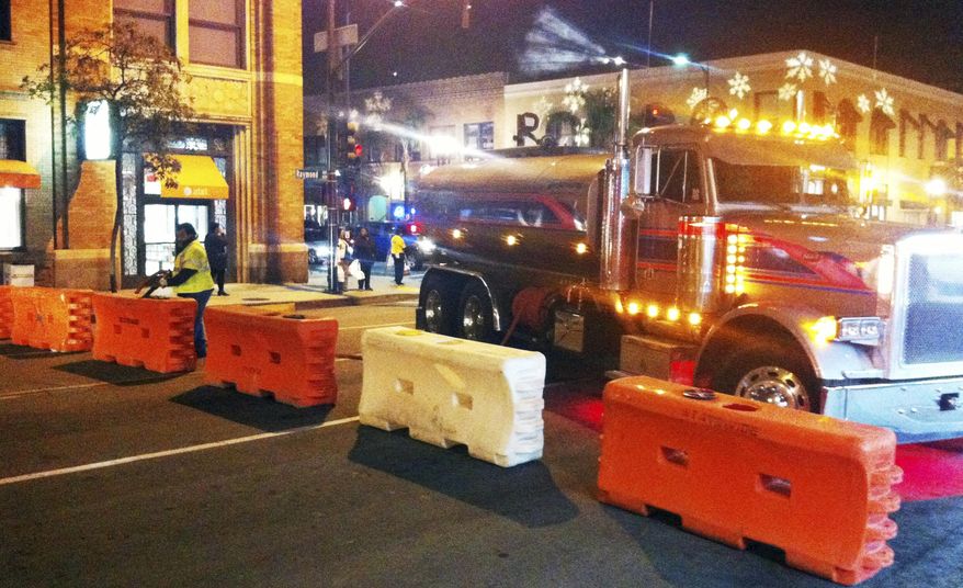 A worker fills barriers with water on one of the cross streets along the route of the Rose Parade on Sunday evening, Jan. 1, 2017, in Pasadena, Calif. The parade is normally held on New Year's Day, but this year will be held on Jan. 2 because of a never-on Sunday tradition. (AP Photo/John Antczak)