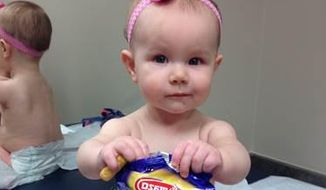 In this photo provided by the Carrie Stevenson, her daughter Estelle holds a bag of peanut snacks in her pediatrician’s office at age 9 months, in Columbus, Ohio. Most babies should start eating peanut-containing foods well before their first birthday, say guidelines released Thursday that aim to protect high-risk tots and other youngsters, too, from developing the dangerous food allergy. The new guidelines from the National Institutes of Health mark a shift in dietary advice, based on landmark research that found early exposure dramatically lowers a baby&#39;s chances of becoming allergic. (Carrie Stevenson via AP)