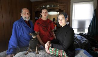 In this Sunday, Dec. 11, 2016 photo U.S. Navy veteran Stephen Matthews, 55, sits for a photograph with his son Alexander, center, and daughter Victoria, right, in the bedroom of a relatives home, in Warwick, R.I. Matthews fell in his driveway in 2015, injuring his neck resulting in him getting laid off from his job. After being evicted he and his wife temporarily lived in their car while his children went to live with a relative. The relative then let Matthews and his wife come too. Matthews said he received a voucher that would pay about two-thirds of his rent, but struggled to find an apartment in Rhode Island where he could afford the balance. He got one in West Warwick, R.I. in late December 2016 after a six-month search. (AP Photo/Steven Senne)